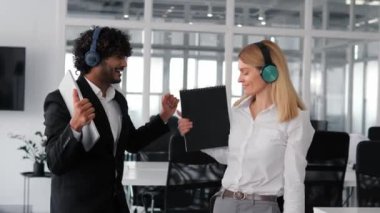 Kablosuz kulaklık takan çeşitli ve neşeli bir grup insan, ortak bir ofis alanında müzik dinlerken ve dans ederken eğleniyorlar. Neşeli erkekler ve kadınlar parti yapıyor.