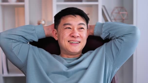 若い幸せな従業員のフリーランスのアジア系中国人のストレッチの閉じる 頭の後ろに手でリラックス 現代的なホワイトオフィスの職場に座って 仕事を休んだ後の笑顔の男 — ストック動画