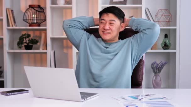 若いコンテンツアジア系中国人のフリーランスは仕事を休み リラックスし 手を頭の後ろに握りしめながらストレッチをしています 彼の休憩中に休息し 充電して 良い気分で笑顔男 — ストック動画