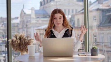 Neşeli, genç, kızıl saçlı kadın, blogcu, vlogger, nüfuzlu biri bulanık şehir manzaralı pencerenin yanındaki bir ofiste oturuyor. Konuşan kız görüntülü konferans görüşmesi web kamerası görüntüsü yapıyor