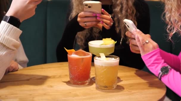 穿着五颜六色衣服的美女们在手机上拍夏季彩色鸡尾酒的照片 最好的朋友们在咖啡馆里玩得很开心 他们在酒吧里为社交媒体拍下了酒精饮料的照片 — 图库视频影像