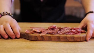 Barmenlerin elleri bir bar veya kafedeki bir grup arkadaş için dilimlenmiş salam üzerine mükemmel bir bira aperatifi koyar. Atmosfer sıcak ve davetkar. Pişmiş et ve içecek aromalı.
