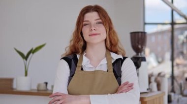 Önlük giymiş, elleri bağlı, beyaz, sağlıklı bir şekilde gülümseyen profesyonel genç bayan, iş yerinde kameraya bakın. Misafirperverlik iyi müşteri hizmetleri, küçük restoran sahibi, kafe personeli portresi