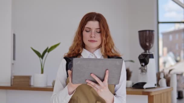 在一家舒适明亮的咖啡店里 成功的女服务员 咖啡店老板正在用平板电脑在线下订单 看着摄像机 餐厅里迷人的红头发女孩的画像 企业家 — 图库视频影像