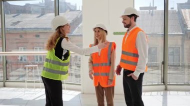 Korumalı yelek ve kasklı bir emlakçı, genç ve başarılı bir çiftle el sıkışıyor, erkek ve kadın, ticari bir mülkün satın alınması veya kiralanması için sözleşme imzaladıktan sonra,