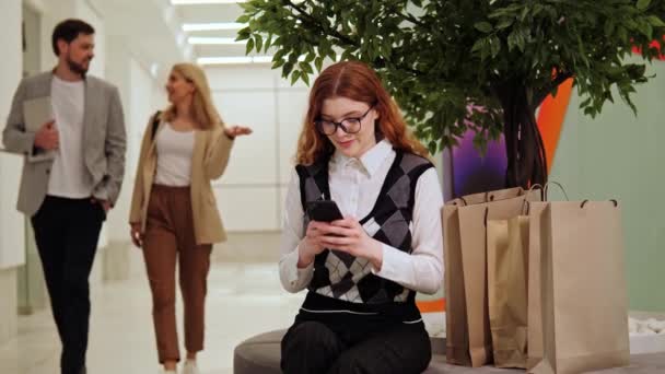 Kızıl Saçlı Gözlüklü Çantalı Bir Kız Alışveriş Merkezinde Cep Telefonuna — Stok video