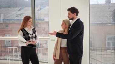 Meşgul yönetici emlakçı kadın emlakçı panoramik pencereli boş bir mülkü birkaç iş adamına kiralamak, satın almak veya satın almak için sunuyor.