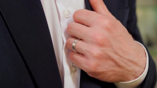美しいホワイトゴールドのリングを持つエレガントな男性の手は クローズアップビューでジャケットの襟に彼の手を置きます このイメージは 優雅さ スタイル 細部への注意を伝えます 正式な訴訟でトレンドビジネスの人々 — ストック動画