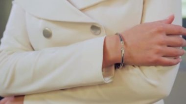 Yakından bakınca, beyaz ceketli güzel sarışın kız bir kuyumcuda poz veriyor, kolye ve küpe deniyor, aynaya bakıyor, sonra da kameraya bakıyor, aksesuarların güzelliğini gösteriyor.