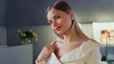 Güzel bir yüzü ve elmas yüzüğüyle mücevher dükkanında poz veren zarif bir kız. Beyaz ceketli sarışın kız alyans takıyor. Mücevher reklamı.