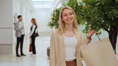 Beyaz bir tişört ve ceket giyen harika gülümseyen güzel bir kız alışveriş merkezinden alışveriş yaptıktan sonra yakın çekim portresi için poz veren el çantaları taşıyor..