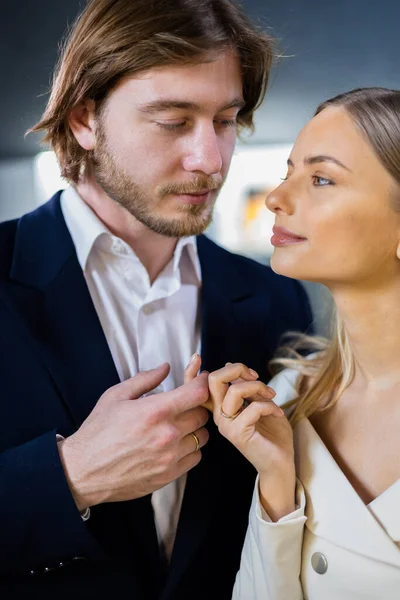 Handsome man in a trendy suit gently holds his girlfriends hand looks into her eyes at a high-end jewelry boutique. Woman has beautifully cared for skin face wears an exquisite diamond gold ring