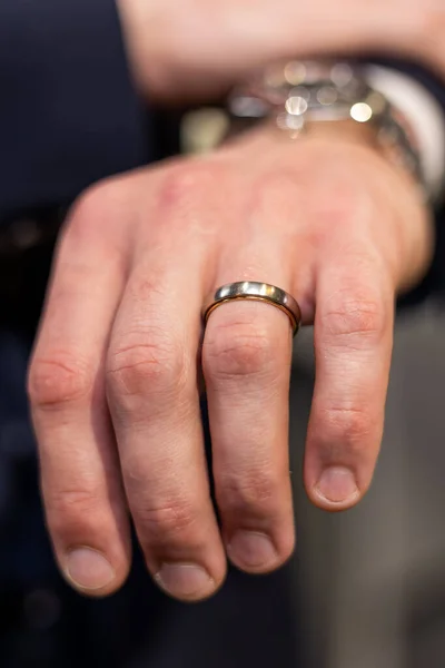 Close-up shot in a jewelry boutique mans hand adorned with a wedding ring and a blurred expensive watch. Focus is on the ring, symbolizing the grooms wedding day and the engagement of the couple