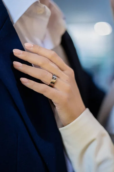 stock image Womans hand adorned with a beautiful precious gold diamond ring holds the collar of her partners jacket in a jewelry salon. The girl and her boyfriend are together on the eve of their wedding