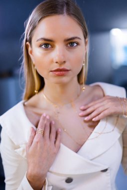 Yüzünde pürüzsüz deri olan beyaz ceketli güzel bir kız ellerinde elmaslar olan altın bir kolye tutuyor. Boynunda elmas kolye olan kız aksesuarlar için bir kuyumcuda.