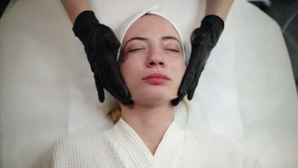 熟練した美容師が肌の細胞の更新を強化するためにクリームマスクを管理し 美容トリートメントの後に癒しの顔マッサージを提供します 美容師は肌の若返りの範囲を提供しています — ストック動画