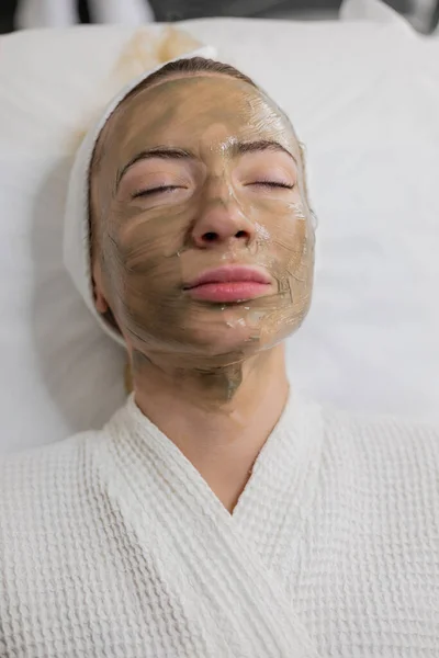 女性は美容クリニックに滞在し 肌を若返らせることを目的とした緑色の顔マスクをスポーツします アクティブクレンジングリフティング治療効果的に戦うにきび拡大毛穴の外観を減少させます — ストック写真