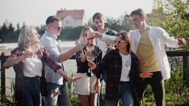 Yakın arkadaşlar göl kenarında şarkı söyleyip dans ediyorlar.