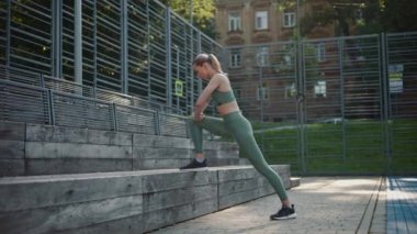 Güzel sporcu kız bacak esnetiyor, tahta bir bankta yaslanıyor.
