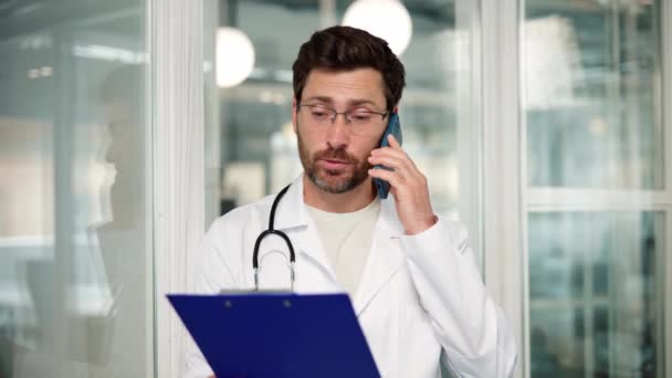 Młody Profesjonalny Lekarz Płaszczu Laboratoryjnym Rozmawiający Przez Telefon Komórkowy Klinice — Wideo stockowe