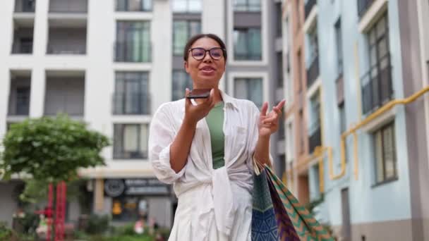 非洲裔美国人吸引人的快乐女人走在户外 在购物街发出愉悦的声音 兴奋的女士通过语音讯息与朋友分享她的黑色星期五兴奋 — 图库视频影像