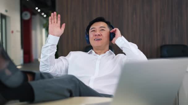 在现代无线耳机中 一个积极英俊的男人一边一边用手跳舞一边唱歌 一边驾驶着音乐 亚洲男性雇主穿着正装 在工作时间喝咖啡休息时玩乐 — 图库视频影像