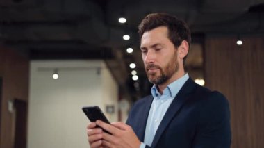 Resmi giyinmiş yakışıklı beyaz adam çalışma alanında duruyor, cep telefonuyla sohbet ediyor ve yüzünü çeviriyor. Esmer beyefendi iletişim için kablosuz teknoloji kullanıyor..