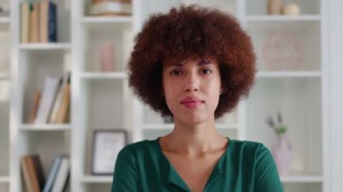 Modern ofiste dikilirken kameraya bakan kıvırcık saçlı kendine güvenen bir kadının portresi. İş yerinde poz veren yeşil bluzlu Afrikalı Amerikalı iş kadını..