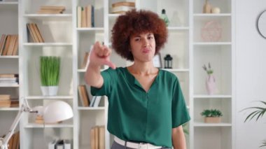 Afro-Amerikan kökenli hoşnutsuz genç bir kadının portresi yeşil bluz giyiyor ve baş parmağını aşağı hareket ettiriyor. Mutsuz bir kadın. Elleri ofiste olumsuz duygular ifade ediyor..