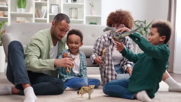 居心地の良いアパートの床で一緒に遊ぶ4人の美しいアフリカ系アメリカ人の家族 2人の息子の魅惑的な想像力を育てるために動物のフィギュアを使用して母親と父親を世話 — ストック動画