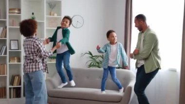 Afro-Amerikan kökenli eğlenceli aktif bir aile şık bir oturma odasında parti veriyor ve dans ediyor. Kaygısız küçük çocuklar kanepede yalın ayak zıplıyorlar ve anne ve babalarıyla evde eğleniyorlar..