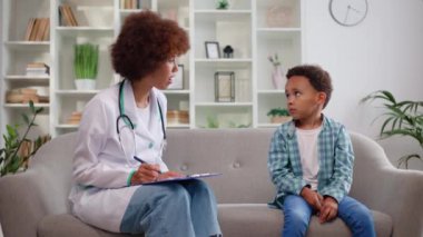 Sevimli bir çocukla randevusu olan ve muayeneyi muayenehanede yapan bir kadın bebek doktoru. Gülümseyen kadın çocukların telaffuzunu kontrol ediyor ve iyi bir hareket gösteriyor..