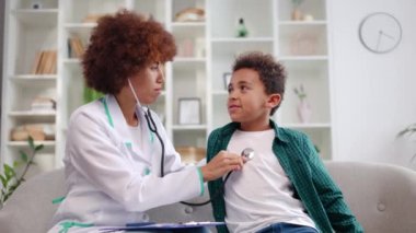 Evdeki check-up sırasında çocukların kalp atışlarını steteskopla dinleyen bir tıp uzmanı. Yakışıklı çocuk doktora bakıyor, derin nefes alıyor ve gülümsüyor. Çocukların sağlık hizmetleri kavramı.