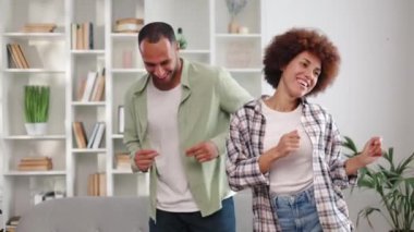 İki aktif Afro-Amerikalı eş kendilerini mutlu hissediyorlar ve evde küçük bir eğlence yapıyorlar. Neşeli kadın ve sıradan giyinmiş adam birlikte gülüyor ve neşeyle dans ediyorlar..