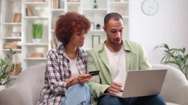 Sıradan giyimli mutlu çift koltukta otururken kablosuz bilgisayardan kredi kartı bilgilerini giriyorlar. Evli Afro-Amerikan halkı birlikte alışveriş yapıyor ve internetten satın almaya çalışıyor..