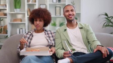 İçerik sahibi Afro-Amerikan kadın son pizza parçalarının tadını çıkarırken adam elinde içkiyle şişeyle geziyor. Genç, neşeli bir çiftin kanepede dinlenirken birlikte eğlenmesi ön planda..