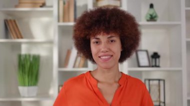 Yüzünde samimi bir gülümsemeyle modern ofise poz veren, şık turuncu bluz giyen Afro-Amerikan genç kadın portresi. İnsan kavramı, iş ve meslek.