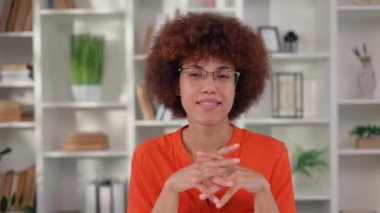 Gözlüklü ve turuncu bluzlu güzel Afro-Amerikan kadın masaüstünde oturuyor ve ellerini çapraz tutuyor. Çağdaş ofiste başarılı bir iş kadını portresi.