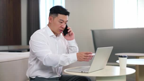 Upptagen Asiatisk Försäljningschef Som Har Telefonsamtal Mobiltelefon När Använder Bärbar — Stockvideo