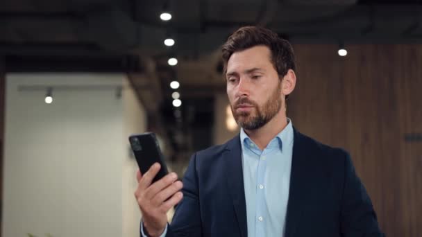 職場に立って スマートフォンでオンラインアプリでビデオ通話をする自信のある企業のプロフェッショナル 外国人投資家との新しい建設プロジェクトの詳細を議論するひげ付き紳士 — ストック動画
