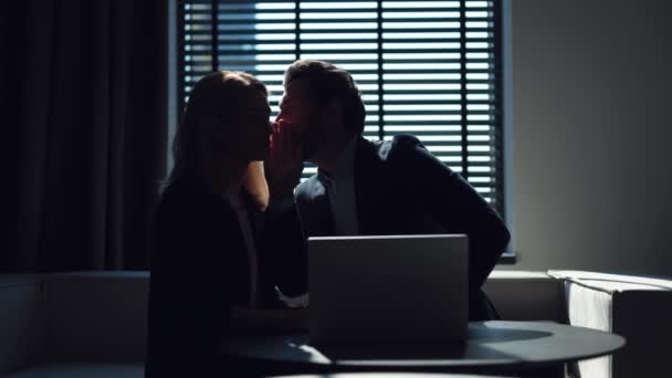 两个穿着正式服装的同事坐在办公室的圆桌旁 工作空间的笔记本电脑和闲聊 有胡子的男人在女人的耳边低声说着令人震惊的消息 并要求保密 — 图库视频影像