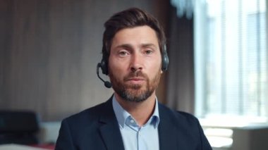 Beyaz sakallı bir adamın portresi. Resmi kıyafetler giymiş. Müşteri hizmetlerinde çalışırken kameraya kablosuz kulaklıkla konuşuyor. İşinin ehli erkek uzmandan müşteri desteği.