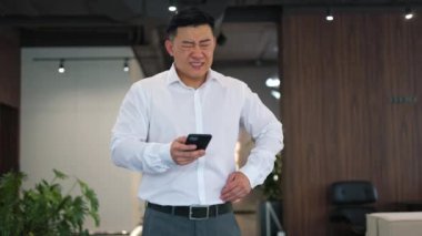 Sağlıksız Asyalı işveren ofisteki akıllı telefondan internete göz atarken ani sancılardan şikayetçi. Genç adam karın bölgesinin sol alt kısmında ani ve şiddetli spazmlar hissederken kaşlarını çatmış..
