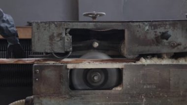 Otomatik testere makinesinin ahşap kütükleri öğütülmüş tahtalara dönüştürdüğü geniş bir kereste fabrikası. Güvenlik eldiveni takan erkek marangozların iş yerindeki yığınla malzemeyi üst üste istiflediği yakın plan. Endüstri kavramı.