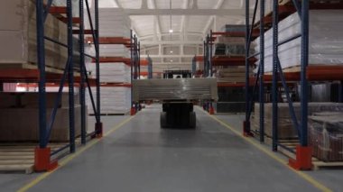 Forklift kullanan cesur bir erkek işçi. Kesik ve düzgünce istiflenmiş tahtalarla depodan odun taşıyor. İnşaat malzemeleriyle dolu uzun ve sağlam raflar. Geniş depolama kavramı.