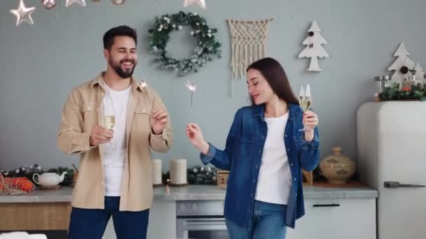 楽しい若いカップルは クリスマスや新年を祝うシャンパンやスパーカーでキッチンで踊っています 男の子と女の子は一緒にお祝いの瞬間を楽しんで 親密な休日の時間を大切にし ワインを飲む — ストック動画