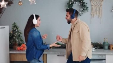 Mutfakta Noel ve yeni yılı kutlayan, kulaklıklarla müzik eşliğinde kaybolan neşeli çift çelenklerle süslenmiş. Kış tatilinin esansını yakalamak eğlenceli ve samimi anlar..