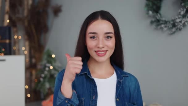ホワイトティーとブルーのシャツで輝く笑顔の幸せな女性は クリスマスの装飾キッチンで親指を上げます お祝いの広告の背景に最適な喜びの承認を表現しています 完璧な笑顔を持っている少女 — ストック動画