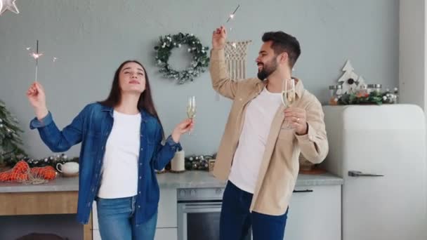 楽しい若いカップルは クリスマスや新年を祝うシャンパンやスパーカーでキッチンで踊っています 男の子と女の子は一緒にお祝いの瞬間を楽しんで 親密な休日の時間を大切にし ワインを飲む — ストック動画