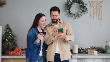 Akıllı telefondan alışveriş yapan ve yılbaşı indirimlerinin tadını çıkaran kredi kartı hediyesiyle alışveriş yapan beyaz bir çiftin portresini yakından çek. Kadın öpüşen koca internetten satın alınmaktan memnun..